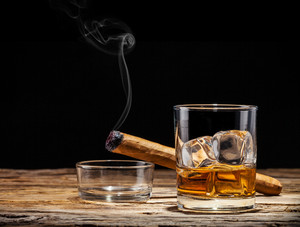 正在燃烧的雪茄旁边的威士忌洋酒图片