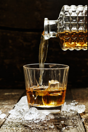往桌面上加了冰块的酒杯倒威士忌的图片